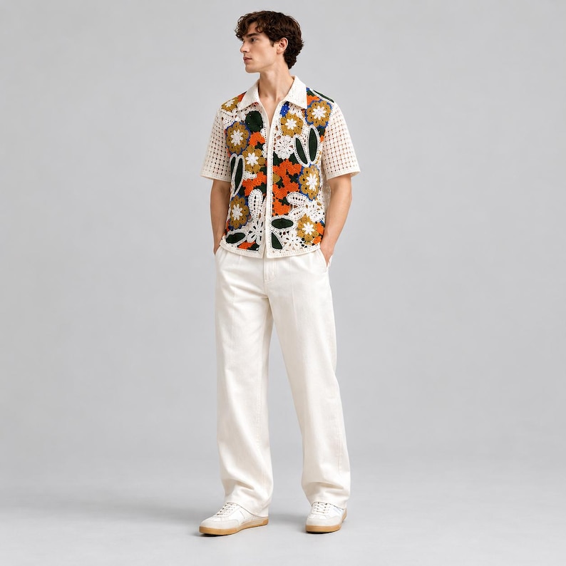 Pode incluir: Uma camisa de manga curta com bot&otilde;es em croch&eacute; cor de creme com um padr&atilde;o floral vibrante em laranja, amarelo, verde e branco. A camisa &eacute; combinada com cal&ccedil;as lisas em branco sujo e t&eacute;nis claros com solas de borracha.