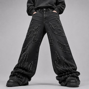 Peut inclure: Jean en denim noir avec une coupe large et un motif de flammes effilochées sur le devant. Le pantalon présente une taille standard avec des passants de ceinture, une fermeture à boutons et des bords effilochés sur les appliques décoratives.