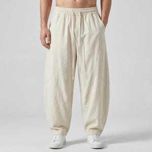 May include: Beige linen pants with a drawstring waist and side pockets. The pants have a relaxed fit and are paired with white sneakers. The fabric appears to be lightweight and suitable for warm weather.