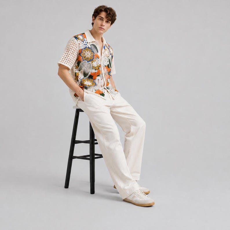 Pode incluir: Uma camisa de manga curta com bot&otilde;es, apresentando costas e mangas em croch&ecirc; na cor creme e um painel frontal com um padr&atilde;o floral vibrante em tons de laranja, azul e verde. A camisa &eacute; combinada com cal&ccedil;as largas na cor creme e t&eacute;nis brancos.