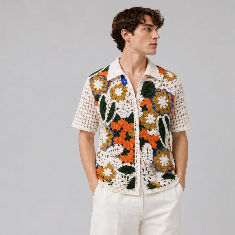 Pode incluir: Uma camisa de manga curta com bot&otilde;es e uma intrincada constru&ccedil;&atilde;o em croch&ecirc;. A pe&ccedil;a apresenta um padr&atilde;o floral vibrante em tons de laranja, amarelo mostarda, verde escuro e branco, com uma textura vazada semitransparente.