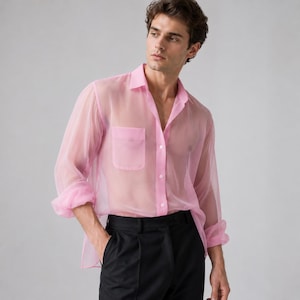 May include: A long-sleeved, button-down shirt in a translucent, light pink fabric. The shirt features a classic collar, a single chest pocket on the left side, and white buttons running down the front placket. The sleeves are loose with buttoned cuffs.