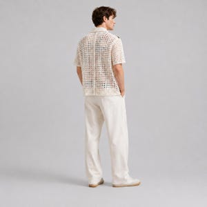 Pode incluir: Uma camisa de manga curta com bot&otilde;es em tom branco sujo, apresentando um padr&atilde;o de croch&ecirc; de malha aberta em forma de grade. &Eacute; combinada com cal&ccedil;as retas a condizer em branco sujo e t&eacute;nis claros, criando um conjunto monocrom&aacute;tico.