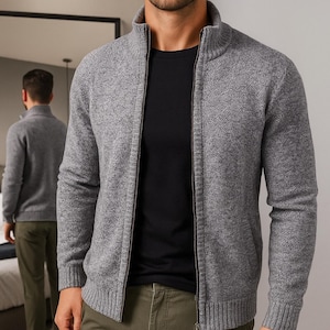 May include: A grey zip-up cardigan with a high collar. The cardigan is worn over a black t-shirt and paired with olive green trousers. The image shows a person in front of a mirror, with a reflection of the same outfit.