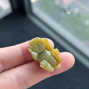 Pu&ograve; includere: Piccola statuetta a forma di rana color giada. La rana &egrave; seduta con le braccia e le gambe distese. La statuetta &egrave; un mix di tonalit&agrave; gialle e verdi, con una superficie liscia e lucida. La rana misura circa 3,8 cm di lunghezza.