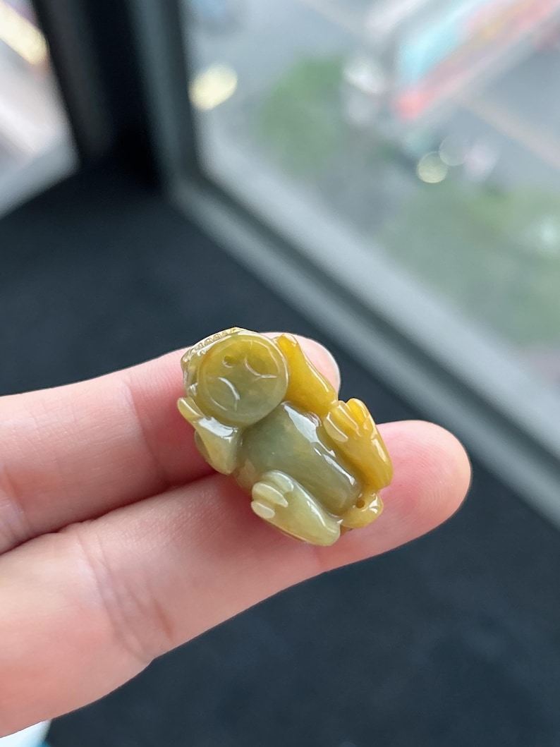 Pu&ograve; includere: Piccola statuetta a forma di rana color giada. La rana &egrave; seduta con le braccia e le gambe distese. La statuetta &egrave; un mix di tonalit&agrave; gialle e verdi, con una superficie liscia e lucida. La rana misura circa 3,8 cm di lunghezza.