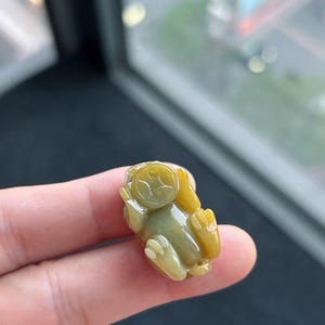 Pu&ograve; includere: Un piccolo ciondolo in giada scolpita a forma di scimmia. Il ciondolo &egrave; principalmente giallo e verde, con dettagli scolpiti sul viso, sulle mani e sui piedi. La scimmia &egrave; seduta, con le mani vicino al viso.