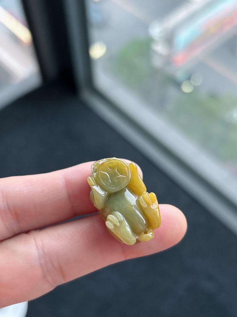 Pu&ograve; includere: Un piccolo ciondolo in giada scolpita a forma di scimmia. Il ciondolo &egrave; principalmente giallo e verde, con dettagli scolpiti sul viso, sulle mani e sui piedi. La scimmia &egrave; seduta, con le mani vicino al viso.