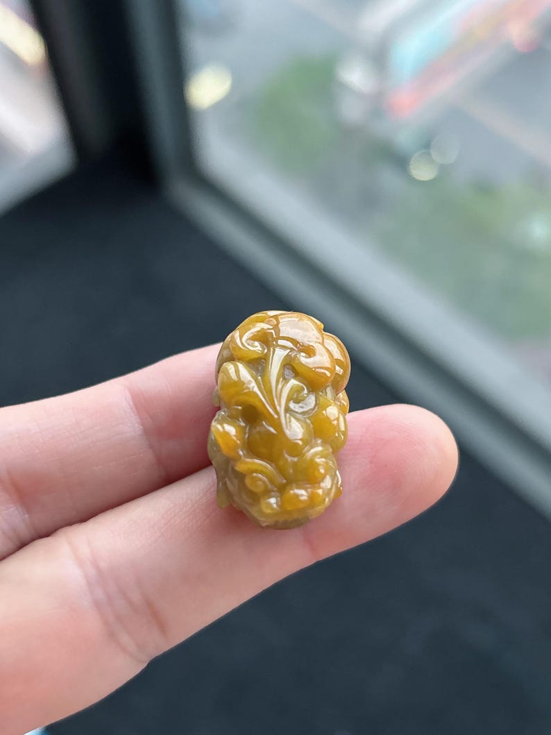 Pu&ograve; includere: Un piccolo ciondolo finemente scolpito, in una calda tonalit&agrave; giallo dorato. Il ciondolo presenta un design dettagliato e a spirale, che potrebbe raffigurare una creatura mitica o un motivo floreale. La superficie lucida riflette la luce.
