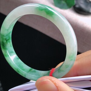 May include: A jade bangle bracelet with a smooth, polished surface. The bracelet features a blend of translucent white and vibrant green hues. The jade is a solid, circular shape, showcasing natural colour variations.