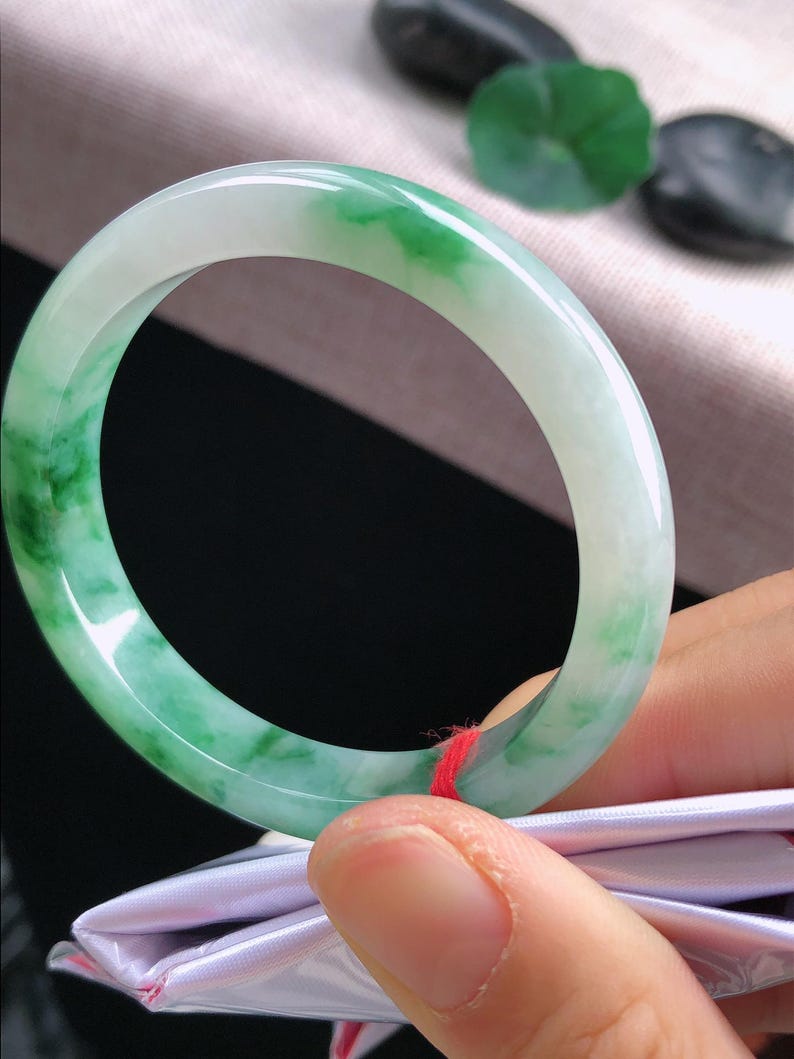 May include: A jade bangle bracelet with a smooth, polished surface. The bracelet features a blend of translucent white and vibrant green hues. The jade is a solid, circular shape, showcasing natural colour variations.
