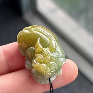 Peut inclure: Pendentif en jade sculpt&eacute; en forme de cr&eacute;ature mythique. Le pendentif est un m&eacute;lange de teintes vertes et jaunes, avec des d&eacute;tails complexes. Un cordon noir est attach&eacute; pour le porter.