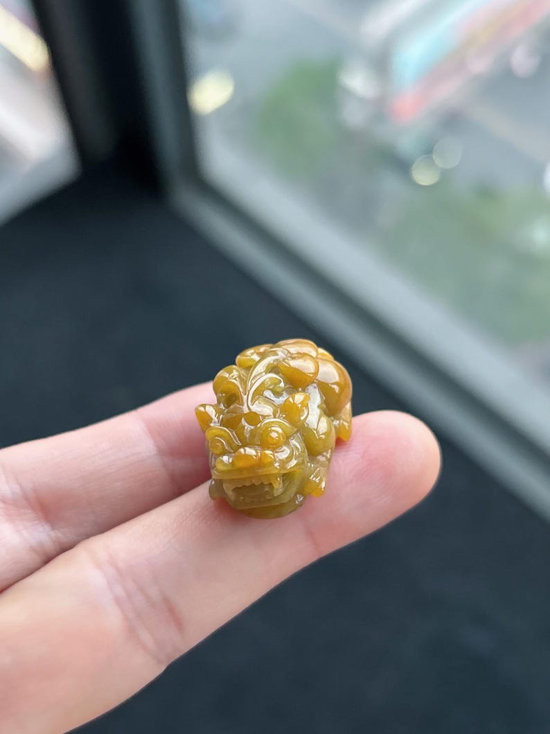 Pu&ograve; includere: Piccola statuetta in giada scolpita, nei toni del giallo e del marrone. La scultura raffigura una creatura mitica con dettagli fini, tenuta tra le dita. La giada ha una finitura lucida e lucente, e l'intaglio mette in risalto l'abilit&agrave; dell'artista.