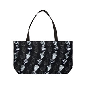 May include: Black tote bag with a repeating pattern of white and black abstract shapes. The bag has a rectangular body with a black handle.