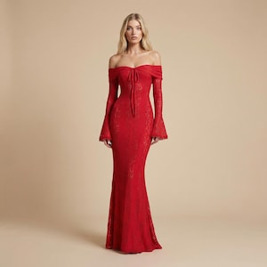 May include: A floor-length, off-the-shoulder red dress with long sleeves and a flared cuff. The dress features a tie detail at the bust and a fitted silhouette that flares out at the bottom. The dress is made of a lace fabric.