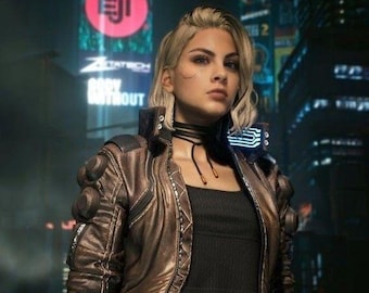 May include: A person with blonde hair wearing a metallic bronze cropped jacket with circular shoulder details, a black ribbed crop top, and black pants with a studded belt. The outfit includes a black choker and a wrist cuff in a dark city setting.