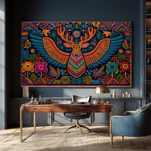 Può includere: Un grande arazzo rettangolare con un design vibrante e colorato di un cervo con ali spiegate, fiori e motivi geometrici. L'opera d'arte è incorniciata e appesa sopra una scrivania in legno con una lampada dorata e una poltrona blu.
