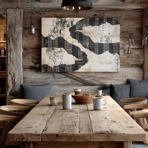 Pode incluir: Uma sala de jantar rústica com uma grande mesa de madeira desgastada e cadeiras. Uma luminária pendente preta pende por cima. Uma grande pintura abstrata com padrões em preto e branco adorna a parede de madeira. A mesa está posta com canecas.