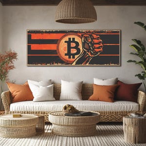 May include: A framed Bitcoin-themed wall art print. The artwork features a Bitcoin symbol and a clenched fist in a retro style, with a black and orange colour scheme. The rectangular print is framed in a light brown colour, suitable for home decor.