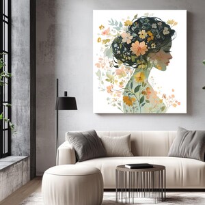 May include: A canvas print featuring a watercolor illustration of a woman's profile, adorned with floral elements. The artwork showcases a woman with flowers in her hair and body, in shades of peach, yellow, and green. The print is displayed in a modern living room setting.