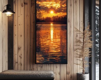 Puede incluir: Una impresión artística vertical enmarcada representa una puesta de sol sobre un lago. El cielo está lleno de tonos naranjas y amarillos, con los rayos del sol rompiendo las nubes. El lago refleja los colores del cielo. La obra de arte cuelga de una pared de madera.