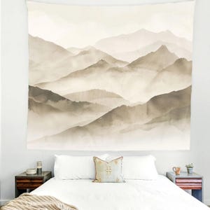 May include: A large, rectangular wall tapestry featuring a watercolor painting of a mountain range in shades of brown and beige. The artwork depicts layered peaks and valleys, creating a sense of depth and tranquility. The tapestry is hanging above a bed.