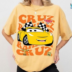 A yellow t-shirt with a graphic of a yellow race car and the text "CRUZ RUM CRUZ" printed on it.