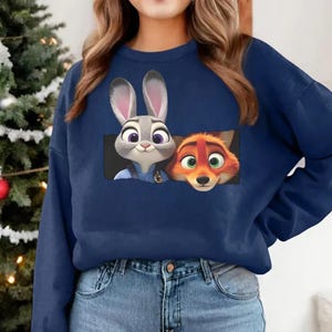 A woman wearing a blue sweatshirt with a graphic of a rabbit and a fox peeking out from the front pocket.