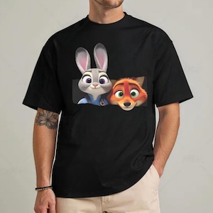 A black t-shirt with a graphic design featuring two cartoon rabbit characters, one gray and one orange, peeking out from behind a fox character.