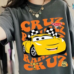 A person wearing a gray t-shirt with a graphic of a yellow race car and the text "CRUZ RUM" printed on it.