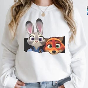 A white long-sleeved shirt with a graphic design featuring two cartoon animal characters, a rabbit and a fox, peeking out from a black frame.