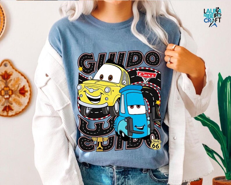 A person wearing a blue t-shirt with a graphic of two cartoon cars, one yellow and one blue, along with the text "GUIDO GUIDE" and "Cars".