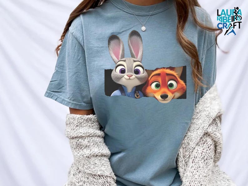 A person wearing a blue t-shirt with a graphic of a rabbit and a fox peeking out from a window.