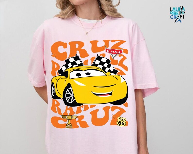 A person wearing a pink t-shirt with a graphic of a yellow race car and racing-related text.