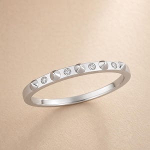May include: A silver-toned ring featuring an alternating pattern of small, conical metal studs and round, clear, faceted stones set along the outer band. The ring has a polished, reflective finish and a slim, circular profile.
