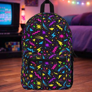 Può includere: Zaino nero con un vivace e colorato motivo ispirato agli anni '80. Il design presenta fulmini giallo neon, triangoli blu, stelle rosa e altre forme geometriche. Lo zaino ha una cerniera nera e una maniglia superiore.