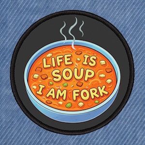 May include: A circular patch with a black edge showing a bowl of orange soup. The text "LIFE IS SOUP I AM FORK" is in yellow. Steam rises from the soup. The patch is set against a blue denim background.