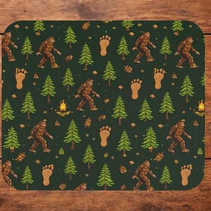 May include: A dark green mousepad featuring a repeating pattern of a brown Bigfoot, footprints, pine trees, and campfires. The Bigfoot is depicted walking. The mousepad has rounded corners.