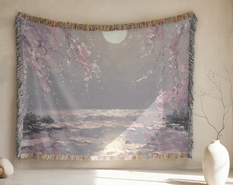 May include: A woven tapestry depicting a tranquil scene with a full moon, water, and pink blossom branches. The colour scheme includes grey, pink, and white tones. The tapestry has a fringed border and is displayed on a wall.
