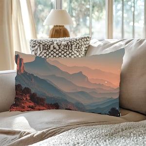 Może przedstawiać: Prostokątna poduszka dekoracyjna z krajobrazem warstwowych gór w odcieniach niebieskiego, pomarańczowego i czerwonego. Poduszka ma malowniczy design, idealny do dekoracji wnętrz.