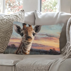 Könnte beinhalten: Rechteckiges Zierkissen mit einem Giraffenporträt vor einem Sonnenuntergang. Die Giraffe hat braune und weiße Markierungen, große Ohren und dunkle Augen. Der Hintergrund zeigt einen farbenfrohen Himmel mit Orange-, Rosa- und Blautönen.