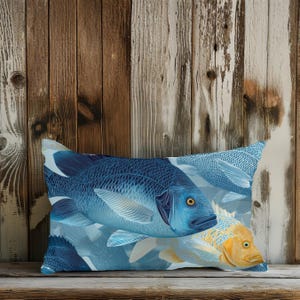May include: Decorative pillow featuring a blue fish design with yellow accents. The pillow has a rectangular shape and is placed on a wooden surface. The fish design is detailed and artistic, with a variety of blue shades.