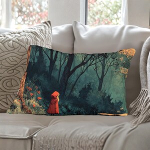 May include: Rectangular decorative pillow featuring a forest scene with a figure in a red hooded cloak. The artwork depicts a dark forest with tall trees, lush greenery, and a touch of orange and gold. The pillow is resting on a gray sofa.