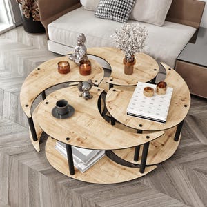 Könnte beinhalten: Ein mehrstöckiger Couchtisch mit hellem Holzfinish und schwarzen Metallbeinen. Der Tisch hat ein Halbmond-Design und ist mit Kerzen, Büchern und dekorativen Gegenständen ausgestattet. Ein Sofa mit Kissen befindet sich im Hintergrund.