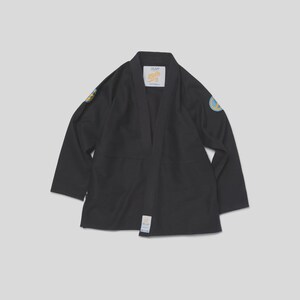 May include: A black martial arts gi jacket featuring long sleeves and a structured collar. The garment includes a white label at the neck with the text "BLU" and a circular patch on each shoulder with blue and yellow graphics. A small white tag is at the hem.