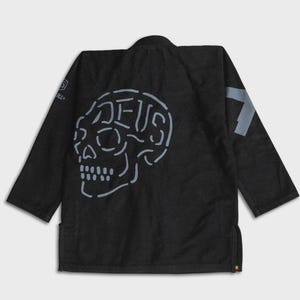 May include: Black martial arts gi with a light blue skull design on the back. The word "DEUS" is integrated into the skull design. A light blue number 7 is on the right shoulder.