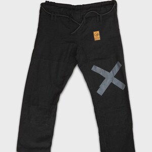 May include: Black martial arts trousers with a grey X graphic on the left leg. The trousers have a drawstring waist and a small, square patch with text. The trousers are made of a durable material.