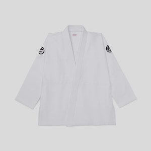 May include: A white martial arts gi jacket featuring long sleeves and a thick lapel. The garment displays a small, circular black logo on each shoulder. The interior neck area contains a small white label with red text, visible at the collar.
