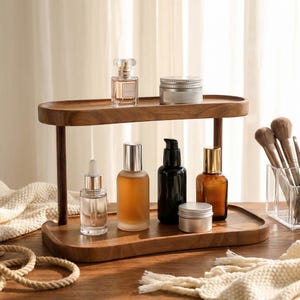 Peut inclure: Un pr&eacute;sentoir en bois &agrave; deux niveaux pr&eacute;sente divers flacons et pots cosm&eacute;tiques. L'&eacute;tag&egrave;re sup&eacute;rieure contient un flacon de parfum et un pot &agrave; couvercle argent&eacute;. L'&eacute;tag&egrave;re inf&eacute;rieure pr&eacute;sente un flacon compte-gouttes, des flacons ambr&eacute;s et noirs et un petit pot.
