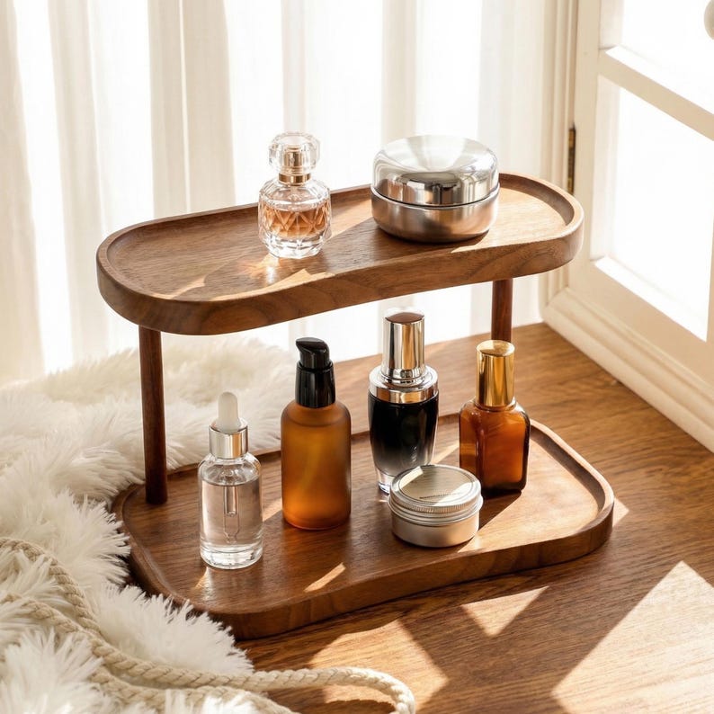 Peut inclure: Un pr&eacute;sentoir en bois &agrave; deux niveaux avec divers produits cosm&eacute;tiques. Le pr&eacute;sentoir est en bois fonc&eacute; et de forme ovale. Les produits comprennent des flacons de parfum, des pots et des flacons avec des compte-gouttes et des pompes.